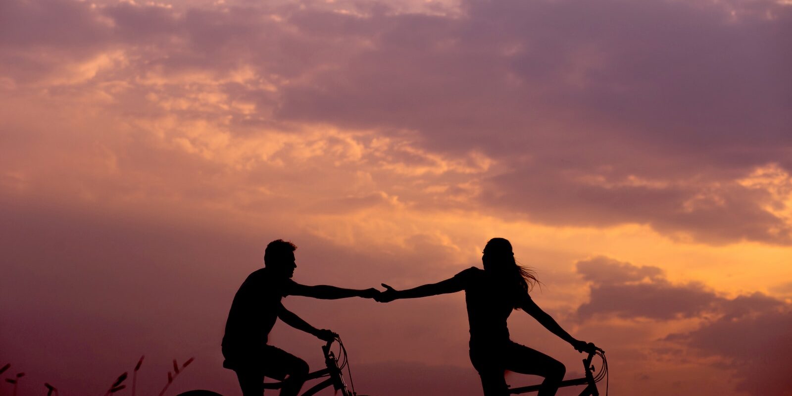 woman on bike reaching for man's hand behind her also on bike